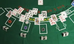 Stół do gry w blackjacka z kartami, żetonami i kostkami. Zasady gry w black jacka są widoczne na zielonym suknie.