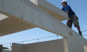 Budowa domu z drewna. Pracownik w kasku montuje drewniane belki. To jak produkcja zdrapek od kuchni, gdzie warstwa ścieralna to solidne drewno.