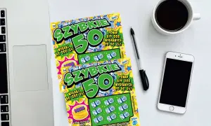 Dwie zdrapki "Szybkie 50" leżą obok laptopa, telefonu i kawy. Czyżby zdrapka jest wygrana?