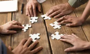 Dłonie składają puzzle, symbolizując wpływ codziennego rozwiązywania szarad na wydajność w pracy biurowej.