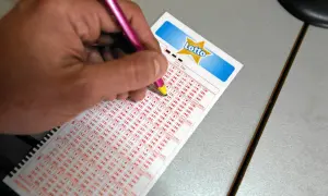 Ręka z różowym długopisem zaznacza liczby na kuponie Lotto. Jak udowodnić że kupon lotto kupiło się wspólnie z partnerem? Wspólne skreślanie liczb to dowód.