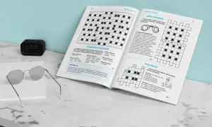 Jak rozwiązywać krzyżówki typu jolka krok po kroku? Na zdjęciu widzimy otwartą książkę z krzyżówkami, okulary i zegarek.