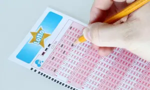 Ręka zaznacza liczby na kuponie Lotto, marząc o jackpot kiedy losowanie.