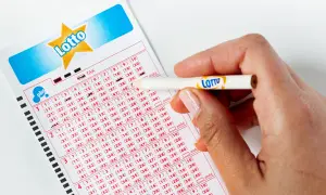Dłoń z ołówkiem z logo Lotto zaznacza liczby na kuponie. Pytanie brzmi: jak długo ważny jest kupon lotto?