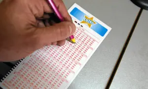 Ręka z różowym długopisem zaznacza liczby na kuponie Lotto. Czy można zagrać w lotto plus nie grając w lotto? Tu szukamy odpowiedzi.