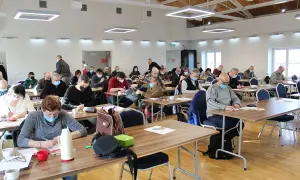 Uczestnicy Mistrzostw Polski w rozwiązywaniu krzyżówek skupieni przy stolikach, każdy z kartką i długopisem. Turniej w toku.