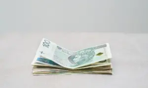 Stos polskich banknotów, w tym 100 zł, leży na jasnym tle. Zastanawiamy się, ile RMF zarabia na loterii.