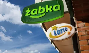 Zielona tablica "Żabka" i biała z napisem "LOTTO" wiszą na tle błękitnego nieba. Czy w każdej Żabce jest lotto?