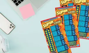 Trzy zdrapki "Super Linie" leżą obok telefonu i słuchawek. Szansa na wygraną 75 000 zł!