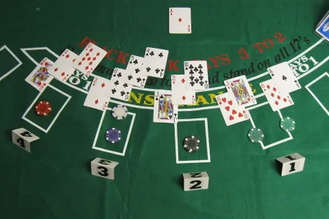 Stół do gry w blackjacka z kartami, żetonami i kostkami. Zasady gry w black jacka są widoczne na zielonym suknie.