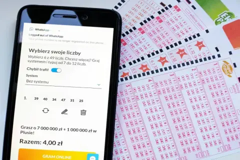 Smartfon z aplikacją do gry w lotto obok zdrapek. Możliwość gry przez SMS i wybierania liczb.