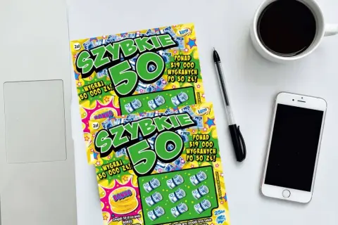 Dwie zdrapki "Szybkie 50" leżą obok laptopa, telefonu i kawy. Czyżby zdrapka jest wygrana?