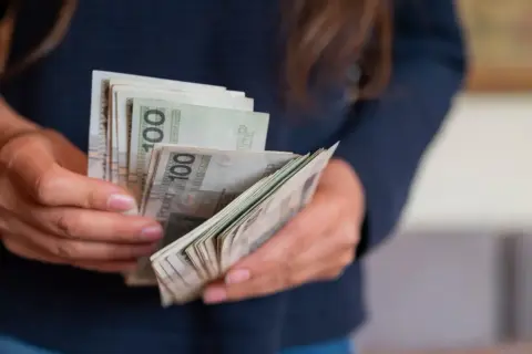 Ręce liczą banknoty 100 zł. Wygrana na zdrapce to darowizna, którą trzeba zgłosić do urzędu skarbowego.