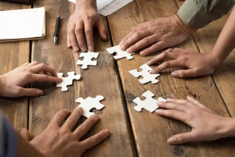 Dłonie składają puzzle, symbolizując wpływ codziennego rozwiązywania szarad na wydajność w pracy biurowej.