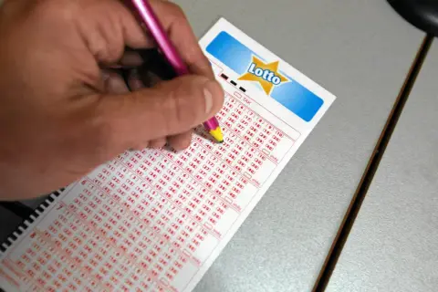 Ręka z ołówkiem zaznacza liczby na kuponie Lotto. Czy na Orlenie jest Lotto? Sprawdź, wypełniając swój kupon!