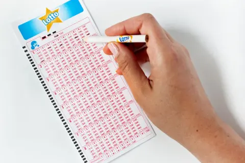 Dłoń z ołówkiem zaznacza liczby na kuponie Lotto. Zastanawiasz się, lotto ile jest do wygrania?