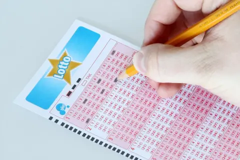 Ręka zaznacza liczby na kuponie Lotto, marząc o jackpot kiedy losowanie.