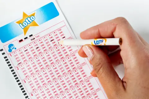 Dłoń z ołówkiem z logo Lotto zaznacza liczby na kuponie. Pytanie brzmi: jak długo ważny jest kupon lotto?