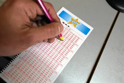 Ręka z różowym długopisem zaznacza liczby na kuponie Lotto. Czy można zagrać w lotto plus nie grając w lotto? Tu szukamy odpowiedzi.