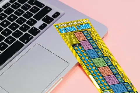 Zdrapka "Extra Linie" leży na laptopie. Czy uda się znaleźć wygrywające symbole i dodatkowe linie?