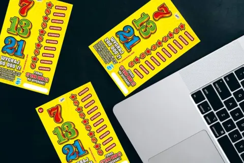 Żółte zdrapki Lotto leżą obok laptopa. Czy sprzedawca w kolekturze wie w której zdrapce jest wygrana?