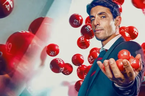 Mężczyzna w garniturze trzyma kulki lotto. Dowiedz się, jak legalnie grać w lotto w dużej grupie znajomych, tworząc syndykat loteryjny.