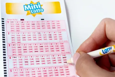 Ręka zaznacza liczby na kuponie Mini Lotto. To pokazuje, jak sprawdzana jest uczciwość bębna i certyfikaty maszyn losujących.