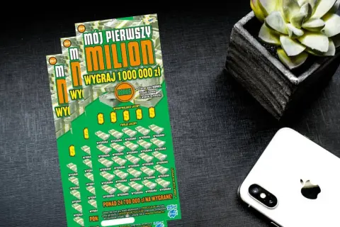 Zielona zdrapka "Mój pierwszy milion" z napisem "Wygraj 1 000 000 zł" leży obok białego iPhone'a i doniczki z sukulentem.
