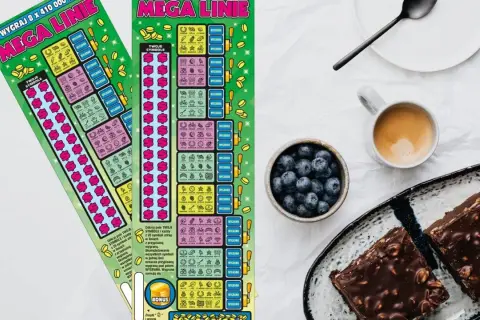 Dwie zdrapki lotto "Mega Linie" leżą obok kawy i ciasta.