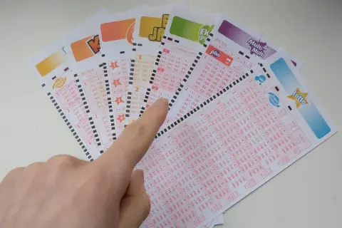Ręka wskazuje na kupony lotto, sugerując, czy systemy do gier liczbowych mogą przewidzieć wyniki loterii.
