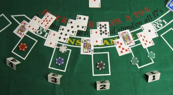 Stół do gry w blackjacka z kartami, żetonami i kostkami. Zasady gry w black jacka są widoczne na zielonym suknie.