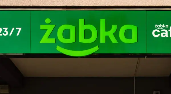 Zielony neon sklepu Żabka z napisem "23/7" i logo "żabka cafe".