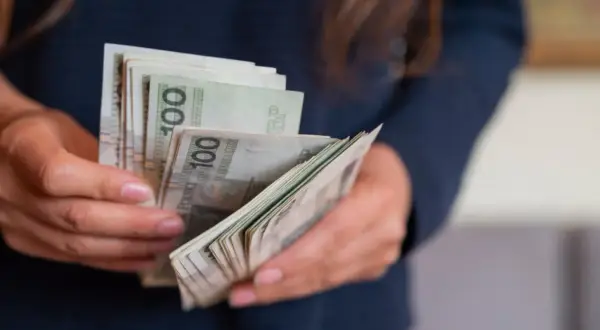 Ręce liczą banknoty 100 zł. Wygrana na zdrapce to darowizna, którą trzeba zgłosić do urzędu skarbowego.