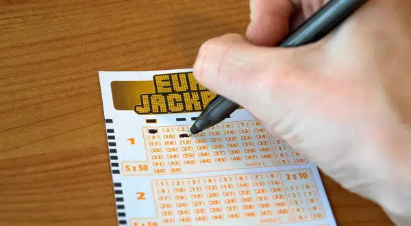 Ręka wypełnia kupon Eurojackpot. Syndykat w Eurojackpot, koszty podziału kuponu systemowego na 10 osób.