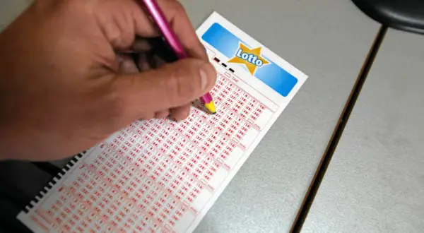 Ręka z ołówkiem zaznacza liczby na kuponie Lotto. Czy na Orlenie jest Lotto? Sprawdź, wypełniając swój kupon!
