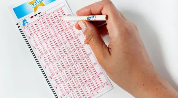 Dłoń z ołówkiem zaznacza liczby na kuponie Lotto. Zastanawiasz się, lotto ile jest do wygrania?