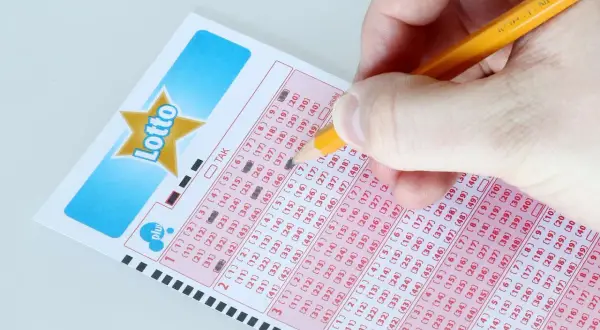 Ręka zaznacza liczby na kuponie Lotto, marząc o jackpot kiedy losowanie.