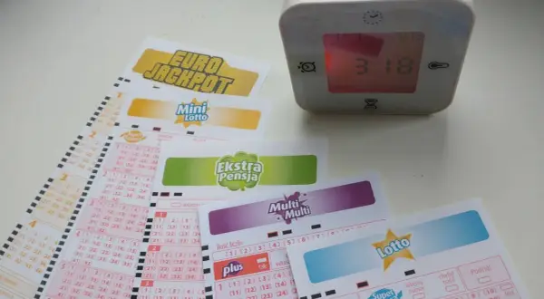 Zegar pokazuje 3:18, a obok leżą kupony gier liczbowych: Eurojackpot, Mini Lotto, Ekstra Pensja, Multi Multi i Lotto. Sprawdź, do której godziny można wysłać lotto w kolekturze.