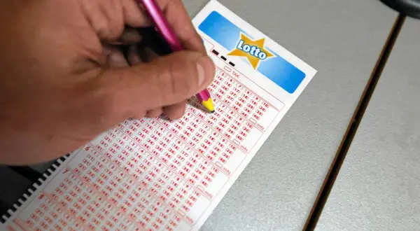 Ręka z różowym długopisem zaznacza liczby na kuponie Lotto. Czy można zagrać w lotto plus nie grając w lotto? Tu szukamy odpowiedzi.