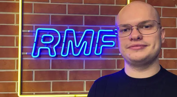 Mężczyzna w okularach stoi przed neonowym napisem RMF FM. Ile jest sejfów w RMF FM? Tego nie wiemy, ale na pewno jest tu dużo dobrej muzyki!