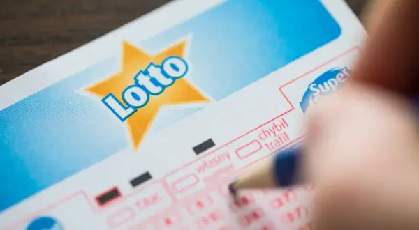Ręka zaznacza liczby na kuponie Lotto. Planujesz grać w lotto w grupie? Dowiedz się, jak sporządzić umowę syndykatu.