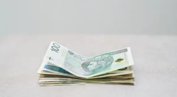 Stos polskich banknotów, w tym 100 zł, leży na jasnym tle. Zastanawiamy się, ile RMF zarabia na loterii.