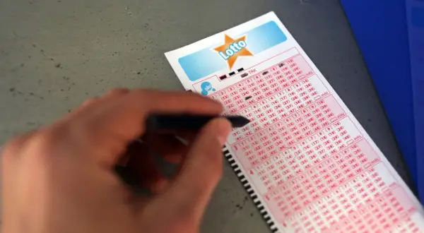 Ręka zaznacza liczby na kuponie Lotto, zastanawiając się, czy najczęściej losowane liczby w lotto statystyki czy mit.