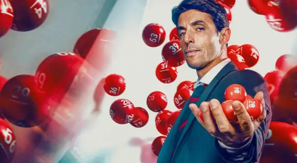 Mężczyzna w garniturze trzyma kulki lotto. Dowiedz się, jak legalnie grać w lotto w dużej grupie znajomych, tworząc syndykat loteryjny.