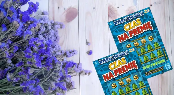 Dwa losy na zdrapki "Czas na premię" leżą obok bukietu fioletowych kwiatów. Zastanawiasz się, ile czasu na odbiór pieniędzy ze zdrapki? Przedawnienie wygranej to ważna kwestia!