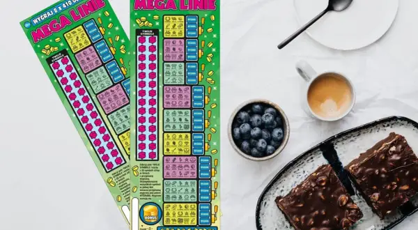 Dwie zdrapki lotto "Mega Linie" leżą obok kawy i ciasta.