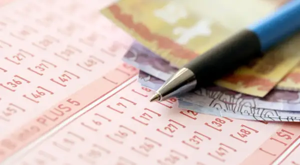 Długopis i banknoty na kuponie lotto. Dowiedz się, jak zorganizować loterię promocyjną w firmie zgodnie z prawem.