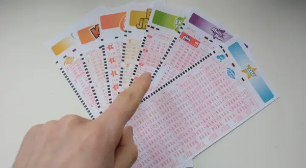 Ręka wskazuje na kupony lotto, sugerując, czy systemy do gier liczbowych mogą przewidzieć wyniki loterii.