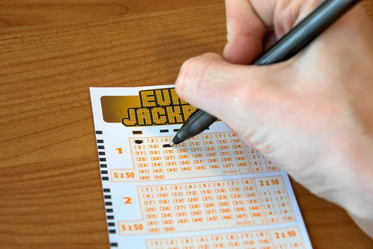Ręka wypełnia kupon Eurojackpot. Syndykat w Eurojackpot, koszty podziału kuponu systemowego na 10 osób.