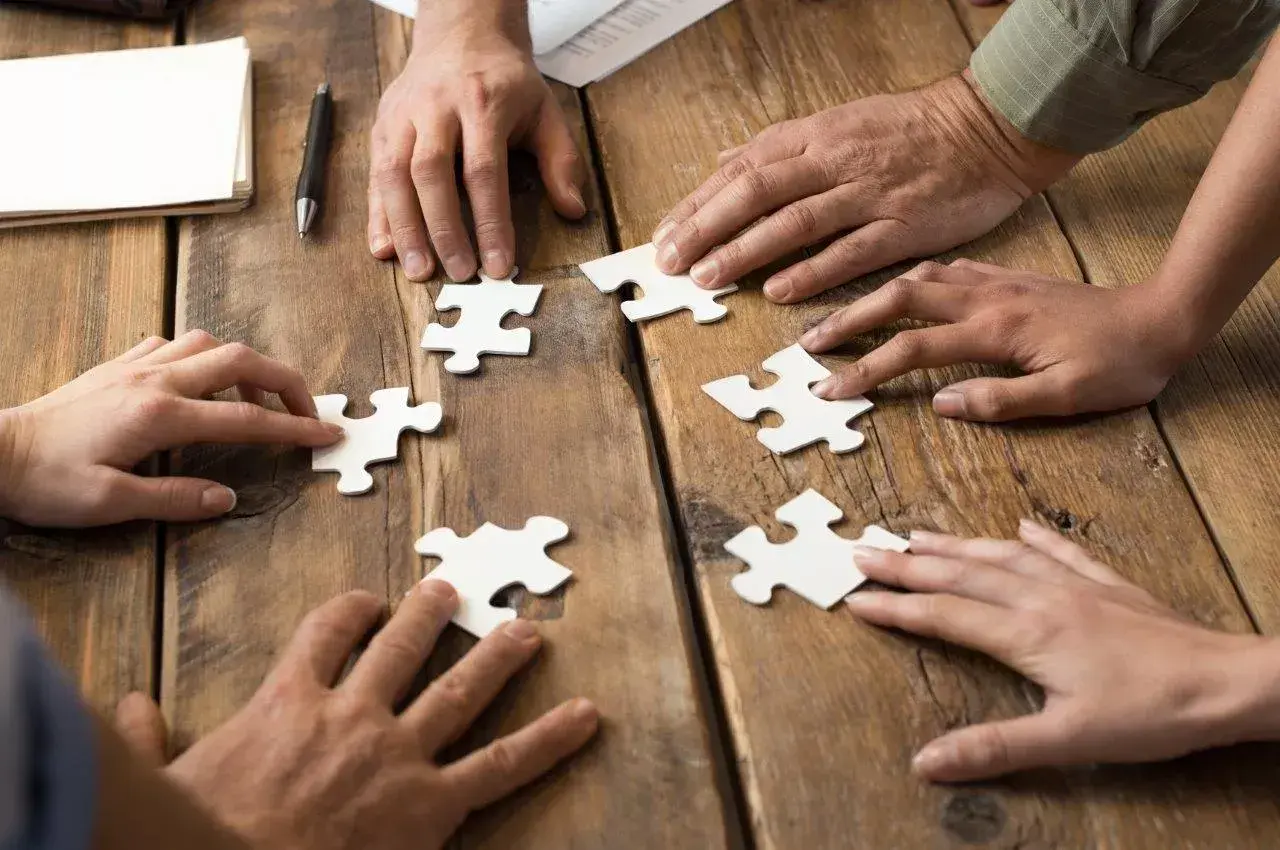 Dłonie składają puzzle, symbolizując wpływ codziennego rozwiązywania szarad na wydajność w pracy biurowej.